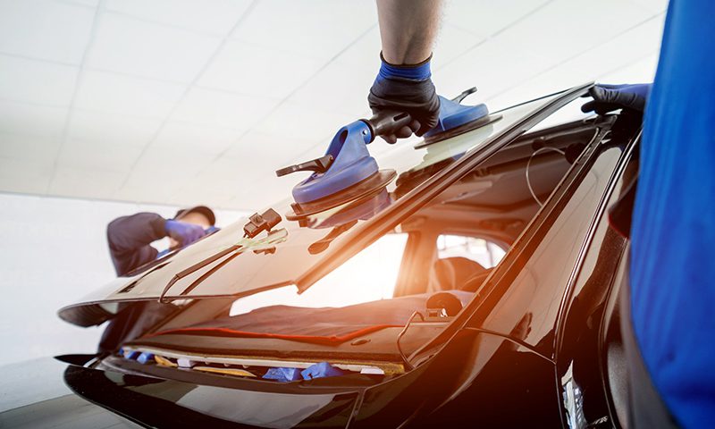 147701262_mE Automobile special workers replacing windscreen or windshield of a car in auto service station garage. Background